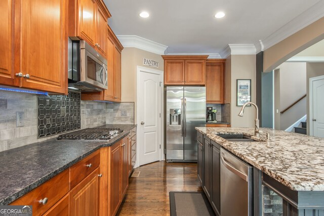 kitchen with a sink, appliances with stainless steel finishes, crown molding, brown cabinetry, and stone countertops