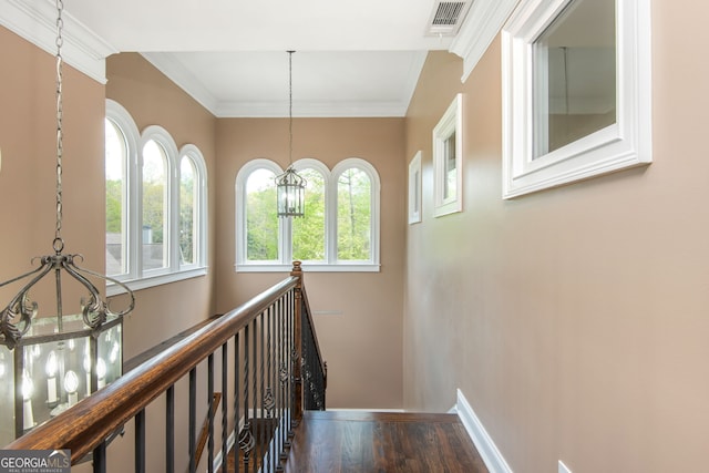 hallway with ornamental molding, visible vents, a chandelier, wood finished floors, and an upstairs landing
