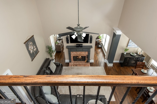 living area with a fireplace, a towering ceiling, a ceiling fan, wood finished floors, and baseboards