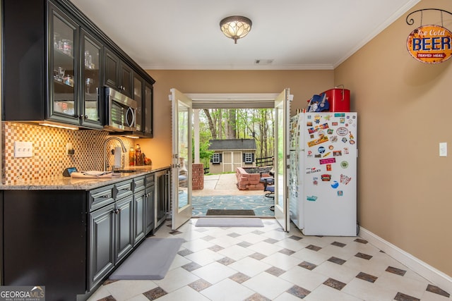 kitchen with freestanding refrigerator, glass insert cabinets, tasteful backsplash, stainless steel microwave, and baseboards