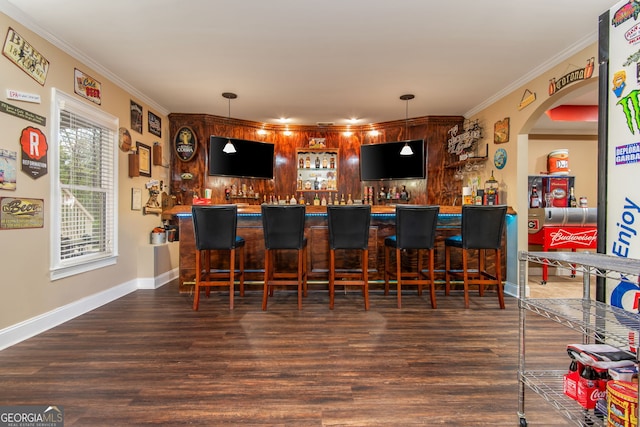 bar with indoor wet bar, ornamental molding, wood finished floors, hanging light fixtures, and baseboards