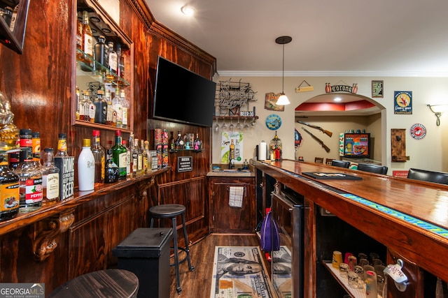 bar featuring ornamental molding, a bar, beverage cooler, and wood finished floors