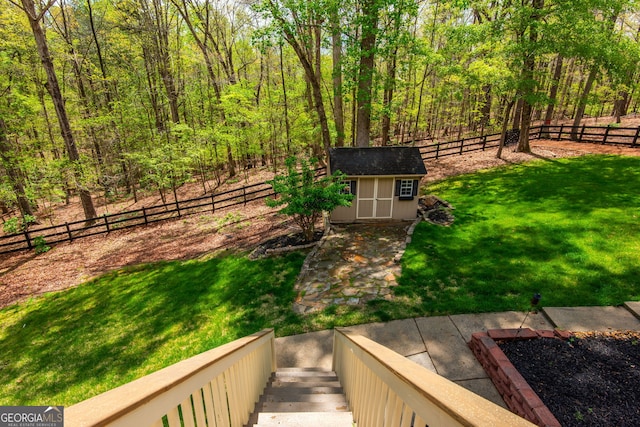 view of yard with a wooded view, a fenced backyard, an outdoor structure, and a storage unit