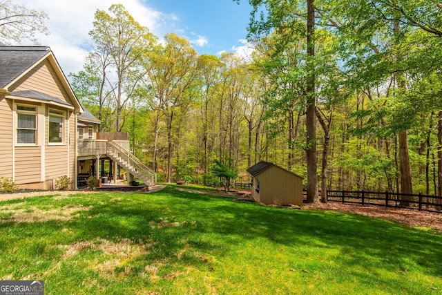 view of yard featuring an outbuilding, a wooden deck, a storage shed, fence, and stairs