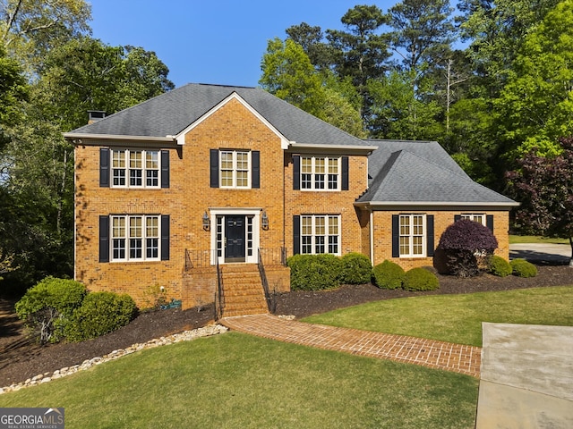 colonial home with brick siding, a front lawn, and a shingled roof