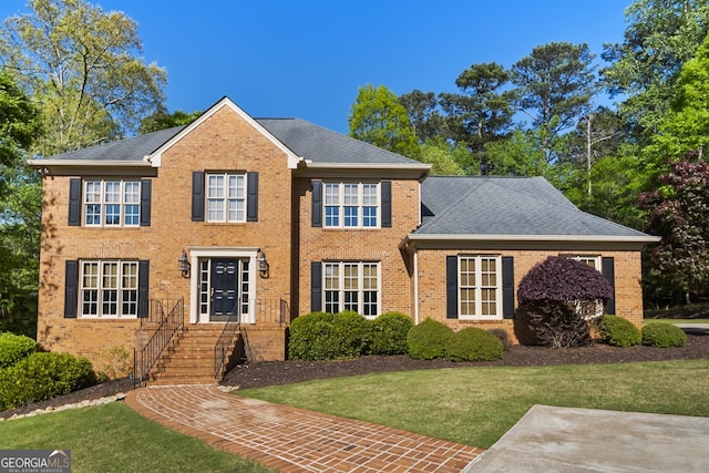 colonial home featuring a shingled roof, a front lawn, and brick siding