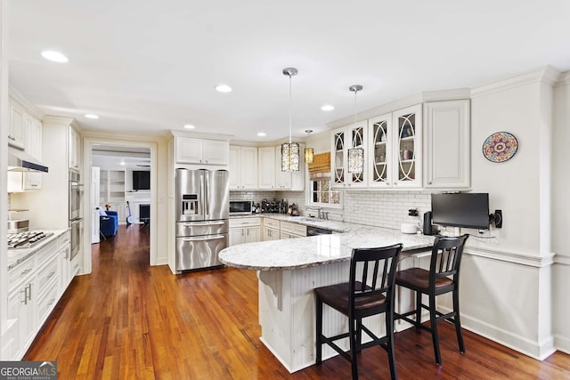 kitchen with light stone counters, a peninsula, backsplash, appliances with stainless steel finishes, and a sink