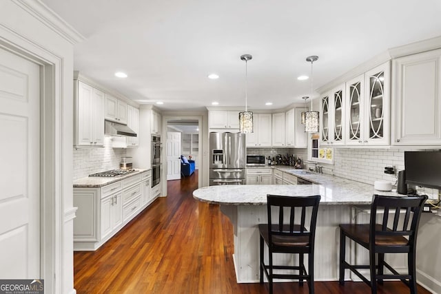 kitchen featuring a peninsula, appliances with stainless steel finishes, under cabinet range hood, a sink, and backsplash