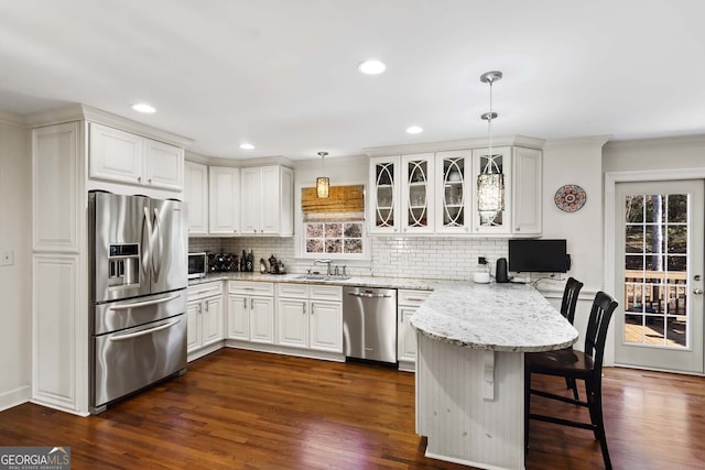 kitchen featuring tasteful backsplash, a kitchen breakfast bar, a peninsula, appliances with stainless steel finishes, and a sink