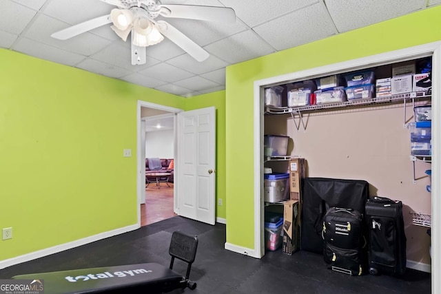 exercise room featuring baseboards, a ceiling fan, and a paneled ceiling