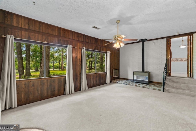 1070 Lovers Lane Rd SE, Calhoun, GA 30701 - unfurnished living room with a wood stove, wooden walls, ceiling fan, a textured ceiling, and carpet