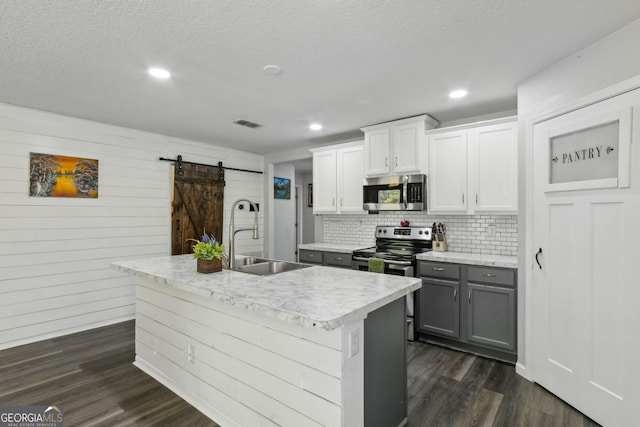kitchen with a barn door, a sink, stainless steel appliances, dark wood-type flooring, and decorative backsplash