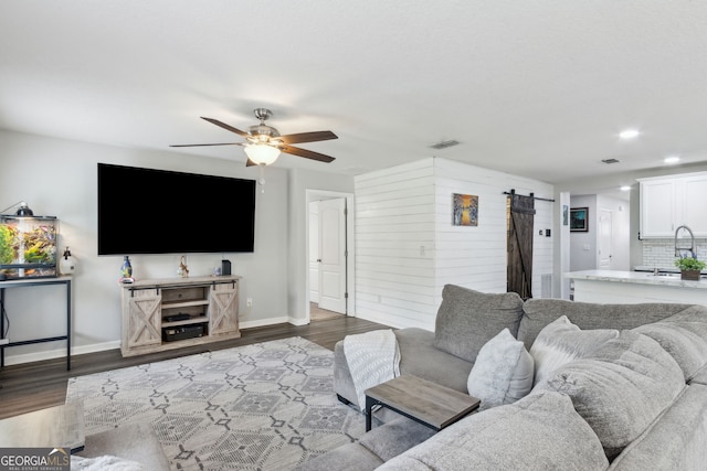 living room featuring a barn door, dark wood-style floors, baseboards, and a ceiling fan