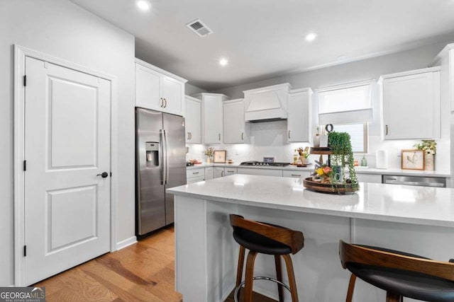 kitchen with a kitchen breakfast bar, white cabinets, visible vents, custom exhaust hood, and stainless steel appliances