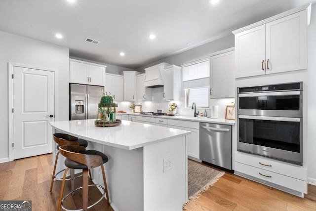 kitchen featuring visible vents, a kitchen island, light countertops, stainless steel appliances, and a breakfast bar area