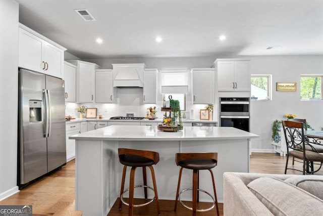 kitchen featuring a breakfast bar, a center island, appliances with stainless steel finishes, light countertops, and custom range hood