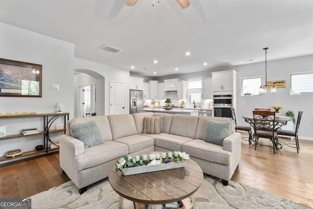 living area featuring arched walkways, a ceiling fan, visible vents, and light wood-type flooring