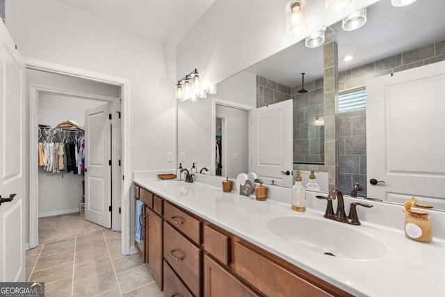 full bath with a spacious closet, double vanity, a tile shower, and a sink