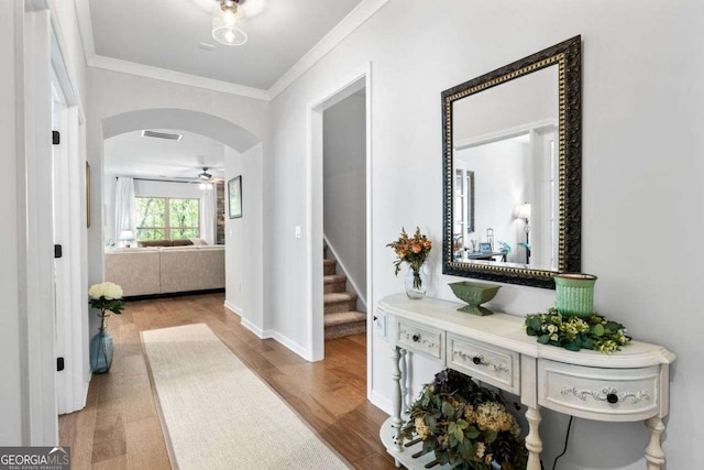 hall featuring stairway, crown molding, visible vents, arched walkways, and wood finished floors