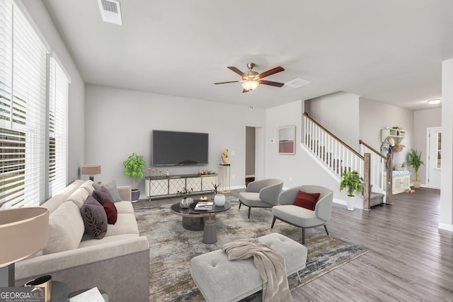 living room featuring ceiling fan, visible vents, stairway, wood finished floors, and baseboards