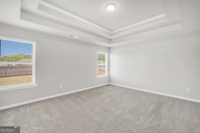 carpeted empty room featuring a raised ceiling, crown molding, baseboards, and visible vents