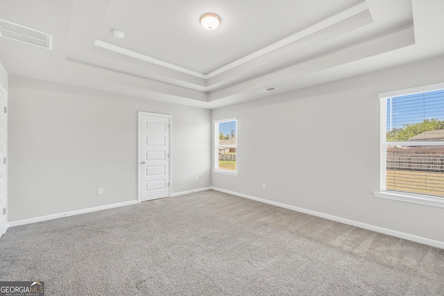 carpeted empty room with a tray ceiling, crown molding, baseboards, and visible vents