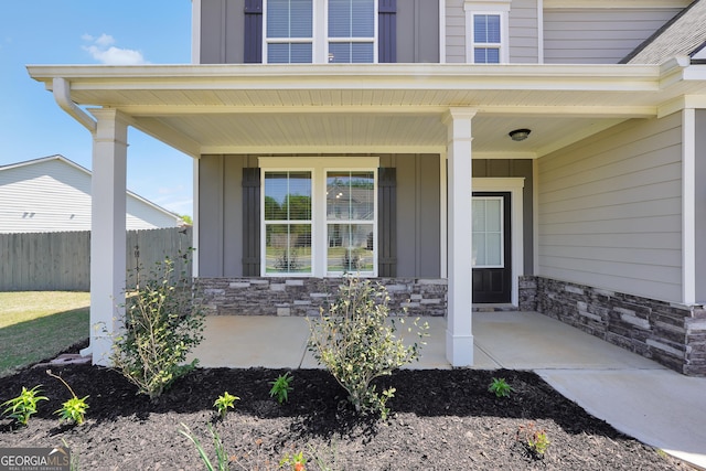 view of exterior entry featuring a porch, board and batten siding, stone siding, and fence