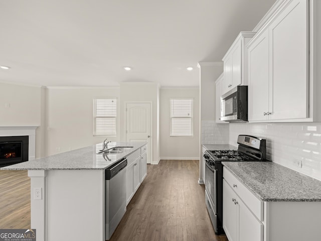 kitchen with appliances with stainless steel finishes, ornamental molding, decorative backsplash, a sink, and wood finished floors