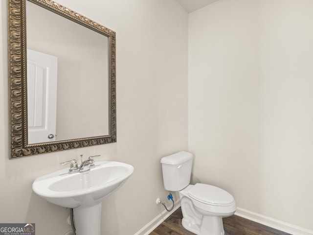 half bath with toilet, wood finished floors, and baseboards