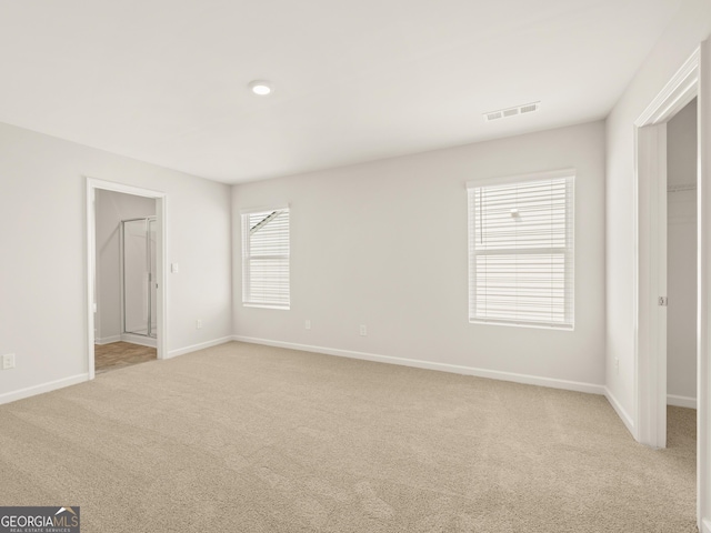 unfurnished bedroom with visible vents, baseboards, a spacious closet, ensuite bath, and light colored carpet