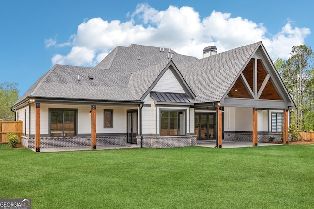 rear view of house featuring a shingled roof, a yard, a patio area, and a chimney