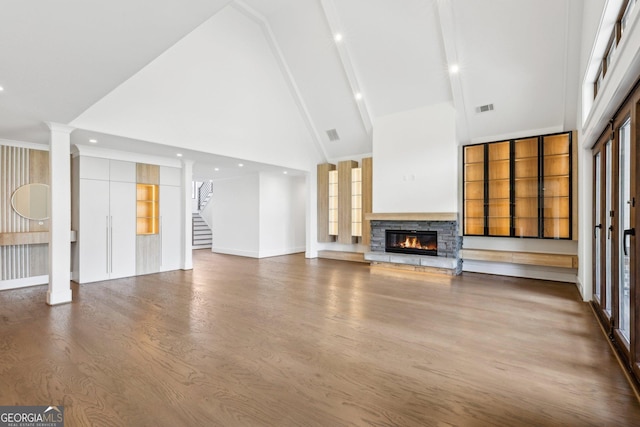 unfurnished living room featuring a stone fireplace, stairway, visible vents, high vaulted ceiling, and wood finished floors