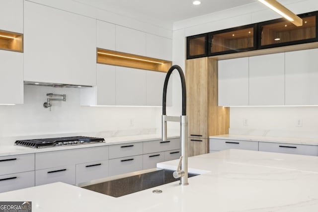 kitchen featuring modern cabinets, light stone countertops, stainless steel gas stovetop, white cabinetry, and a sink