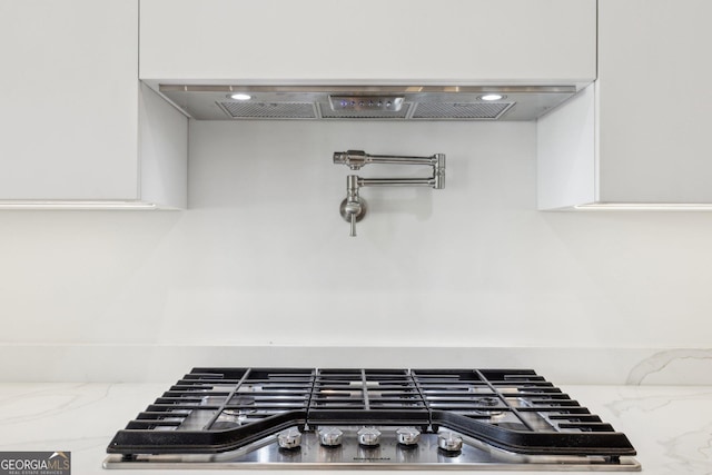 room details featuring stainless steel gas stovetop, white cabinetry, light stone counters, and ventilation hood