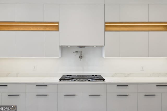 kitchen with light stone countertops, stainless steel gas cooktop, modern cabinets, and white cabinetry