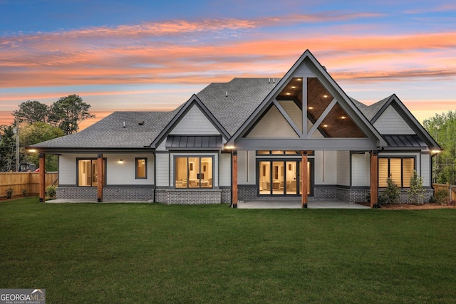 back of property at dusk featuring a shingled roof, a yard, metal roof, a patio, and a standing seam roof