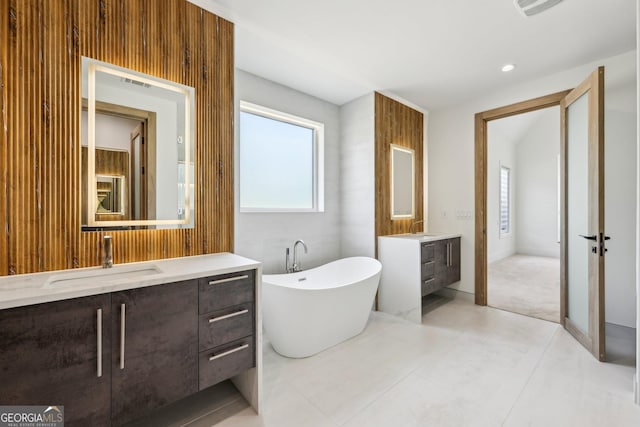 full bath featuring a freestanding bath, two vanities, visible vents, and a sink