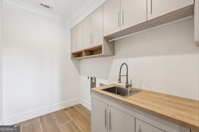 laundry area with visible vents, baseboards, a sink, cabinet space, and light wood-style flooring