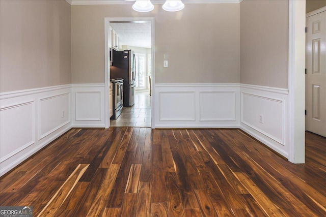 unfurnished dining area with a wainscoted wall, dark wood-style flooring, ornamental molding, and a decorative wall