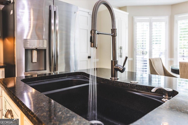 kitchen featuring a sink, stainless steel fridge, and dark stone countertops