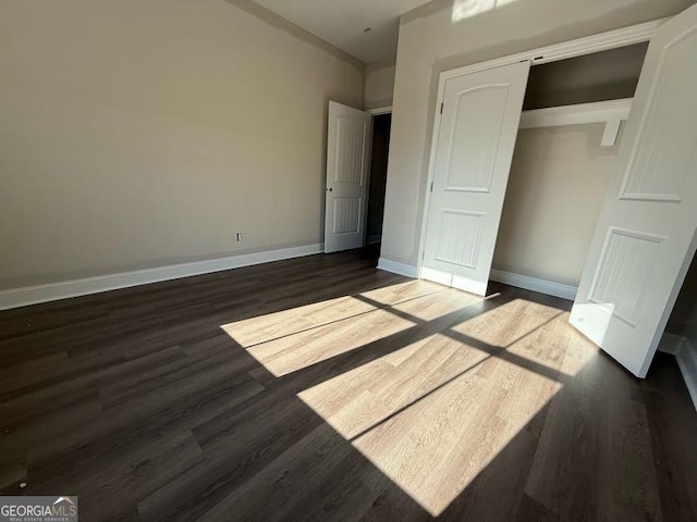 unfurnished bedroom with baseboards, a closet, and dark wood-type flooring