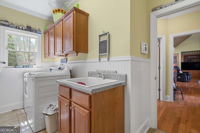 laundry room with a sink, light wood-style floors, wainscoting, cabinet space, and washing machine and clothes dryer