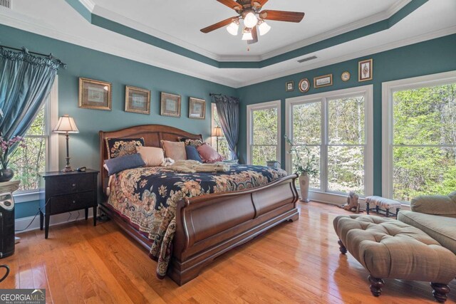 bedroom with crown molding, visible vents, a tray ceiling, and wood finished floors