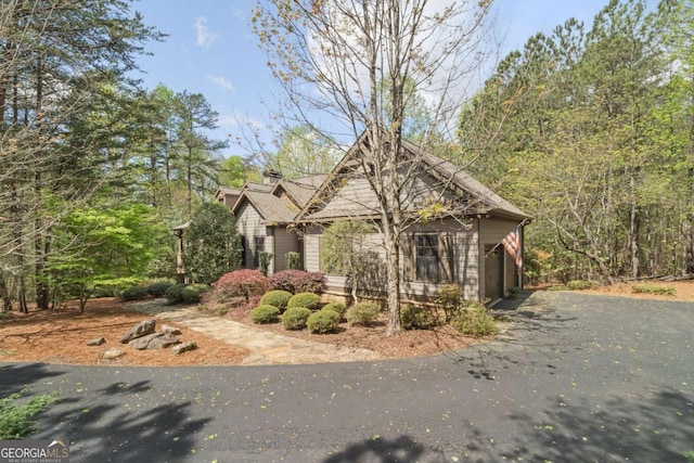 view of property exterior featuring an attached garage, a chimney, and driveway