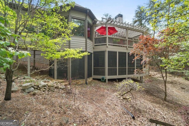 back of house with a sunroom, a chimney, and a pergola