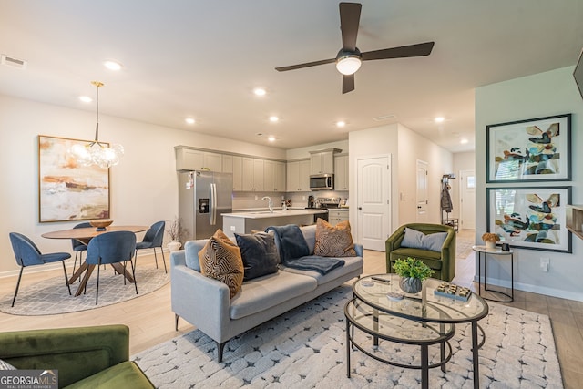 living room with light wood-style flooring, ceiling fan with notable chandelier, baseboards, and recessed lighting