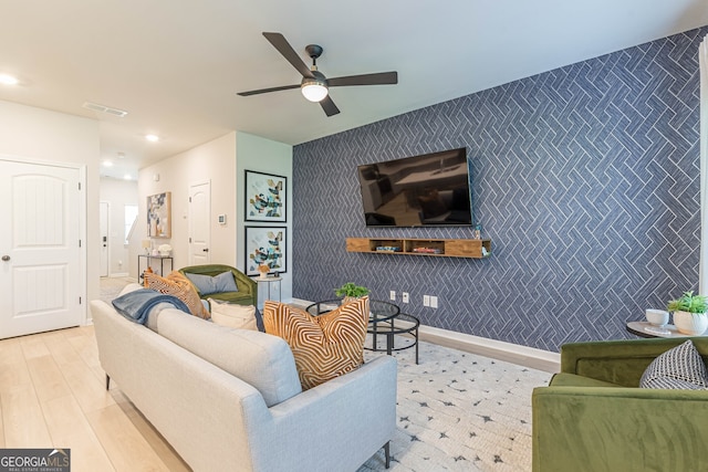 living area with visible vents, a ceiling fan, an accent wall, and wallpapered walls