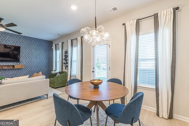 dining area with ceiling fan with notable chandelier, light wood-style flooring, an accent wall, visible vents, and baseboards