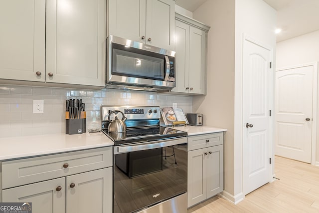 kitchen featuring tasteful backsplash, light countertops, appliances with stainless steel finishes, light wood-style floors, and gray cabinets