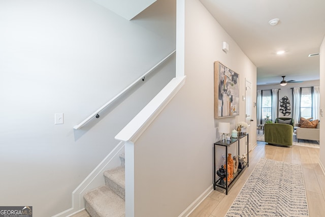 staircase with wood finished floors, ceiling fan, and baseboards